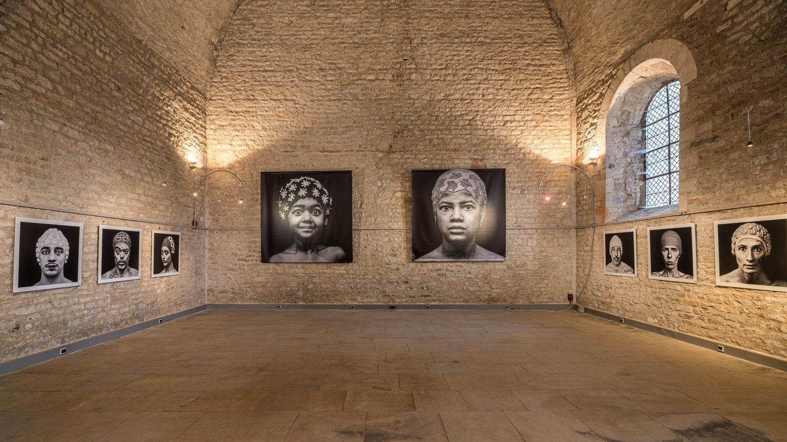 Exposition de portraits accrochés dans un espace en pierre.